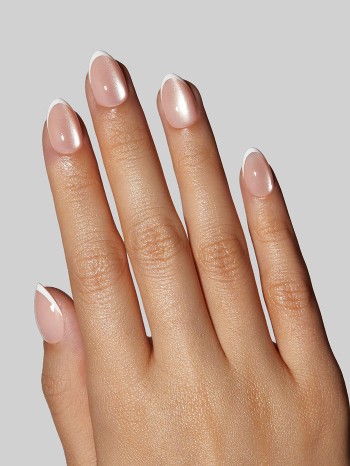 Close-up of a hand with light pink press-on nails on a neutral background