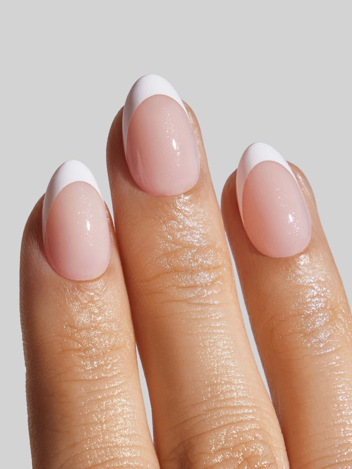 Close-up of a hand with French Tip press-on nails on a light gray background