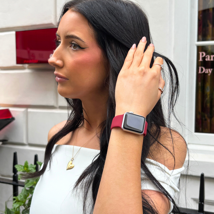 Woman with long dark hair wearing a white top and a red Coconut Lane Apple Watch strap stands outside by a white building.