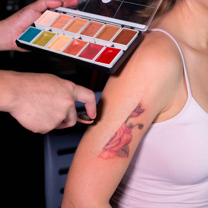 Artist applying tattoo cover-up on upper arm beside open flesh tone alcohol-activated palette
