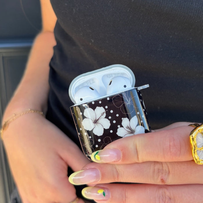 Mono Flora AirPods case with a floral pattern held by a hand with green-tipped nails and a gold ring.