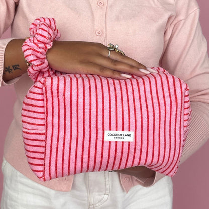 Coconut Lane Towel Makeup Bag in cherry stripe pattern held with a matching scrunchie and pink cardigan.