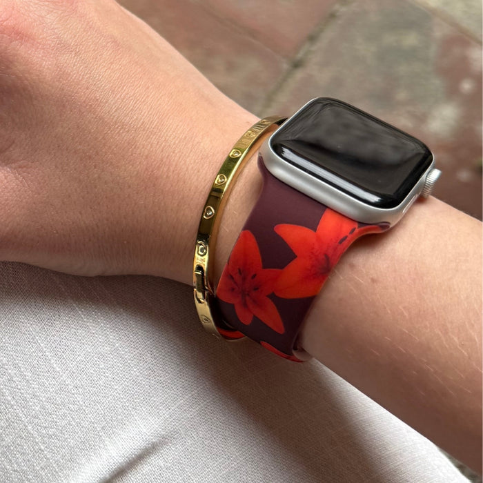 Wrist wearing Coconut Lane Cinnamon Lily Apple Watch strap with gold bracelet on white fabric.