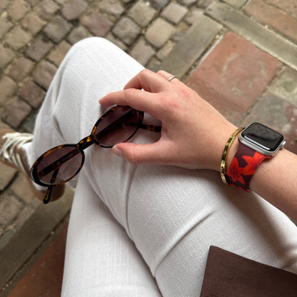 Cinnamon Lily Apple Watch strap with brown and white floral pattern, worn by person in white pants on cobblestone path.