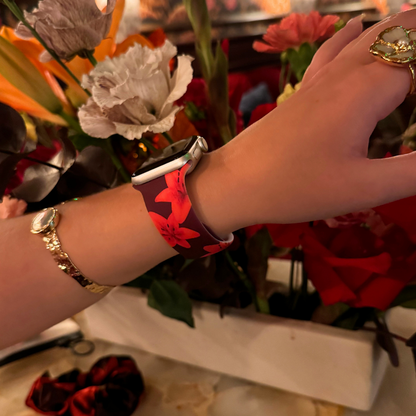 Hand wearing Coconut Lane Cinnamon Lily Apple Watch strap with floral pattern, shown in front of a bright flower bouquet.