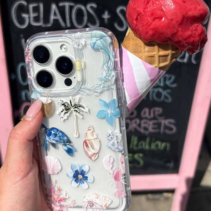 Clear Coconut Lane phone case with a beach girl design, held next to a strawberry ice cream cone by a gelato shop sign.
