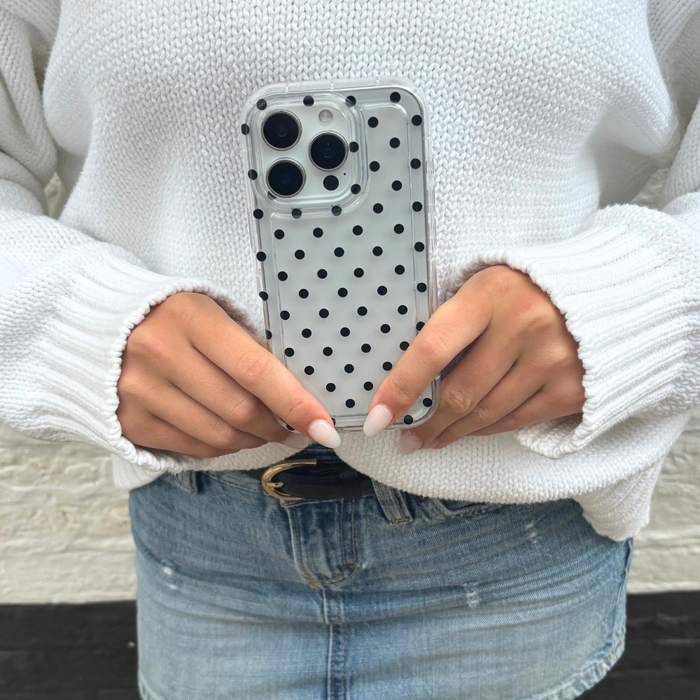 Clear phone case with black polka dots held by a person in a white sweater and denim skirt.
