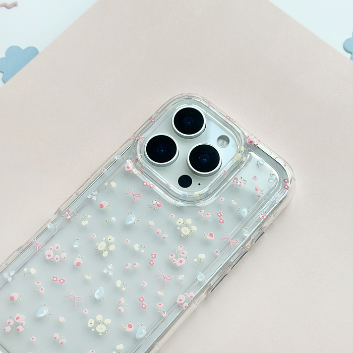 Clear phone case with pink flowers and bows pattern, displayed on a pale pink background.