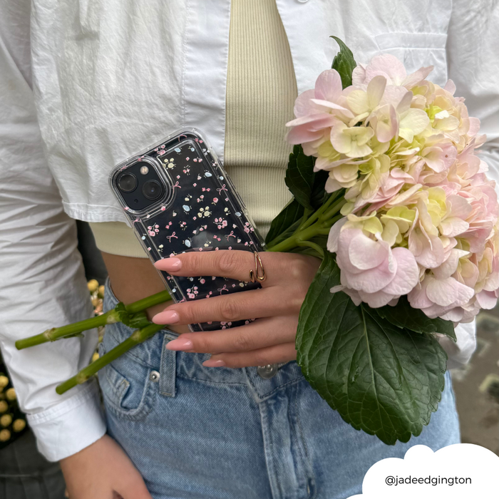 Woman in a white shirt and jeans holds pink hydrangeas and a phone with a pink floral Bows in Bloom case.