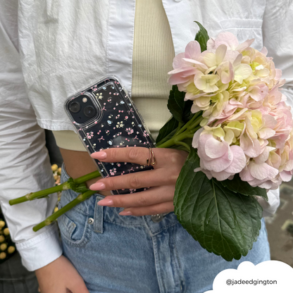 Woman in a white shirt and jeans holds pink hydrangeas and a phone with a pink floral Bows in Bloom case.