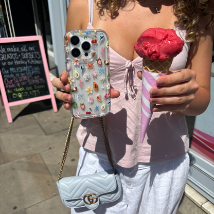 Woman in a pink top outside a shop holds a pink ice cream cone and a clear Coconut Lane phone case with Calypso Club design.