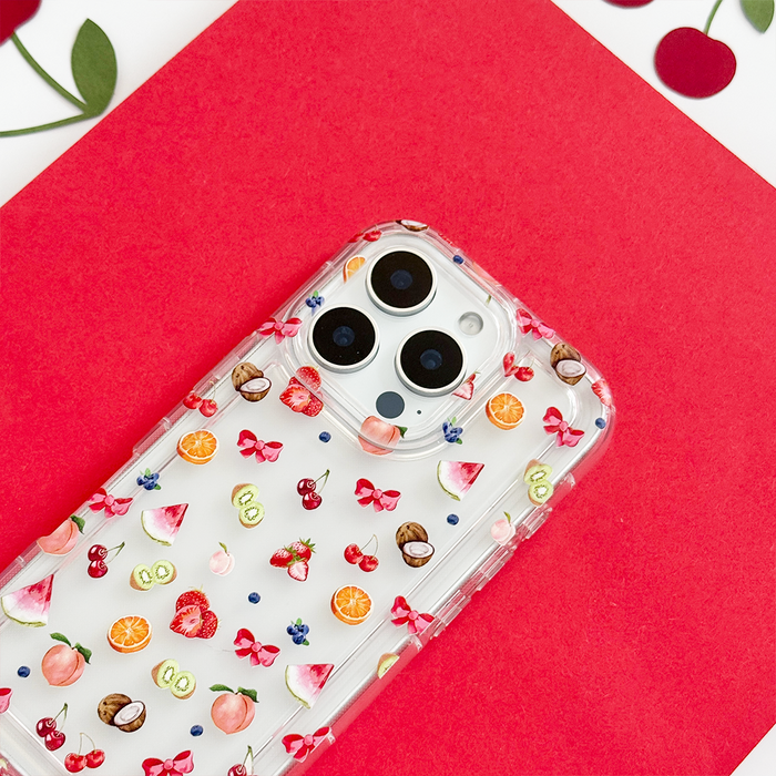 Clear phone case with colorful fruit and red bows on white, displayed against a bold red background.