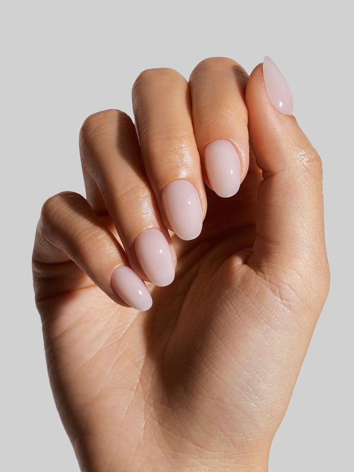 Close-up of a hand with light pink press-on nails on a neutral background