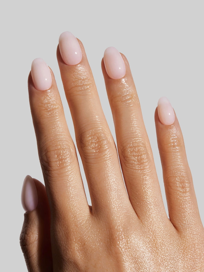 Close-up of a hand with light pink press-on nails on a plain background