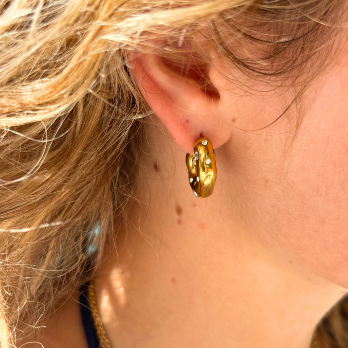 Textured gold hoop earrings with small clear stones worn by a person.