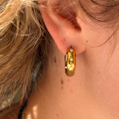 Gold hoop earrings with small gemstones, worn on an ear with light brown hair.