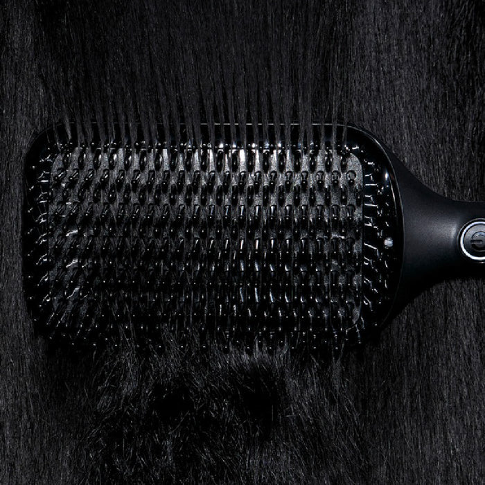 Black paddle hairbrush on a dark textured surface