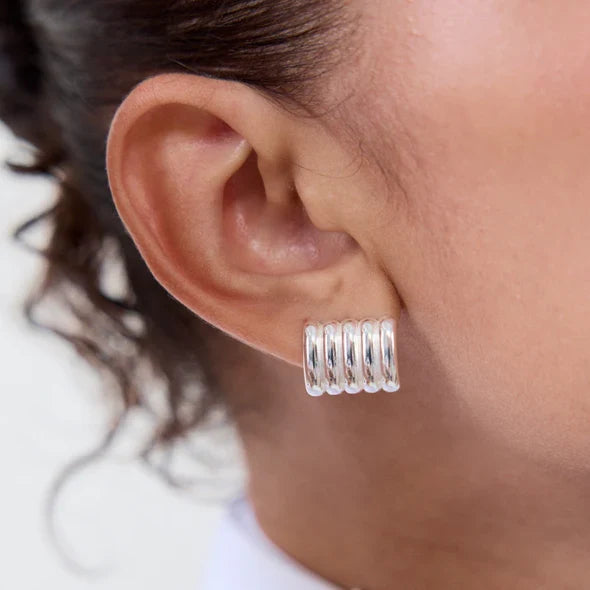 Silver hoop earrings worn by a person with a neutral background