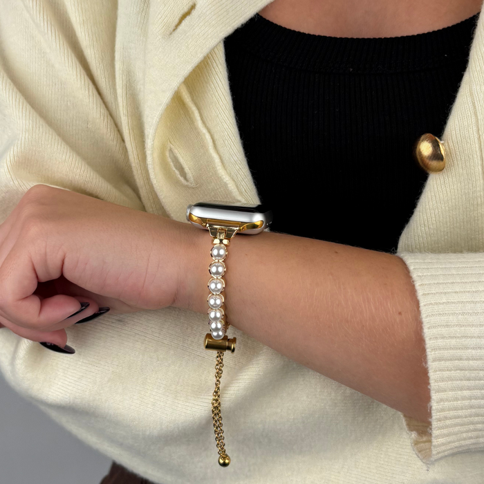 Gold Coconut Lane Isla Pearl Apple Watch strap on woman’s wrist, styled with a black top and cream sweater.
