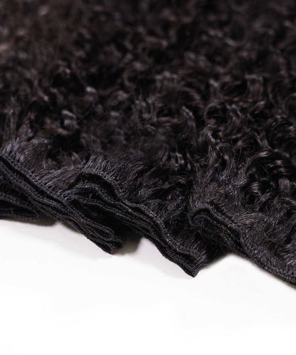 Close-up of several bundles of curly, virgin dark brown or black hair extensions with visible stitching on the wefts, on white surface.