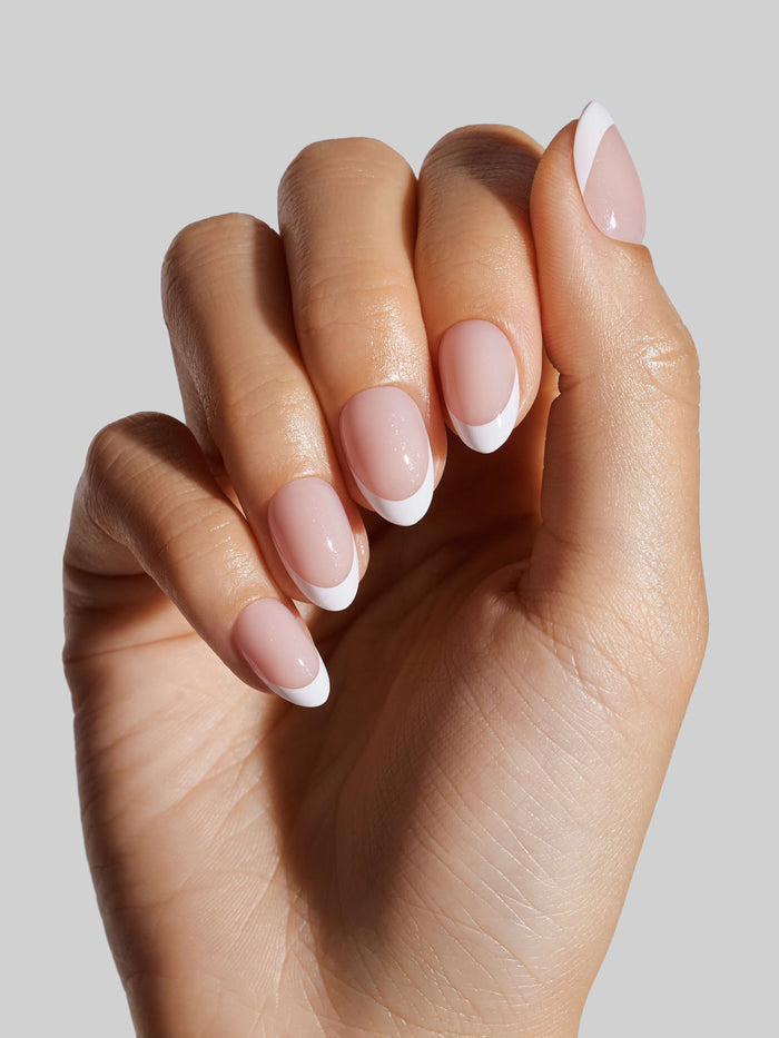 Hand with French Tip press-on nails on a light gray background