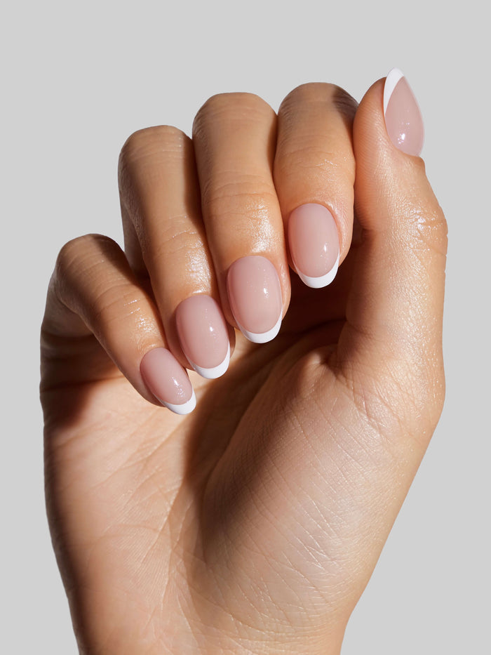 Close-up of a hand with French Tip press-on nails on a neutral background