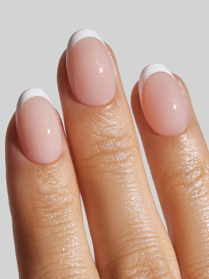 Close-up of a hand with French Tip press-on nails on a plain background