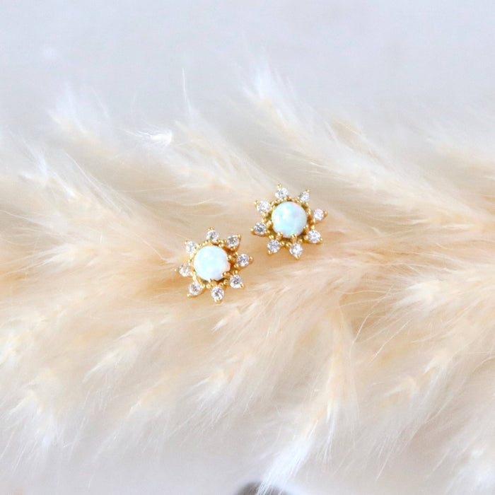 Pair of gold earrings with opal stones on a fluffy white surface