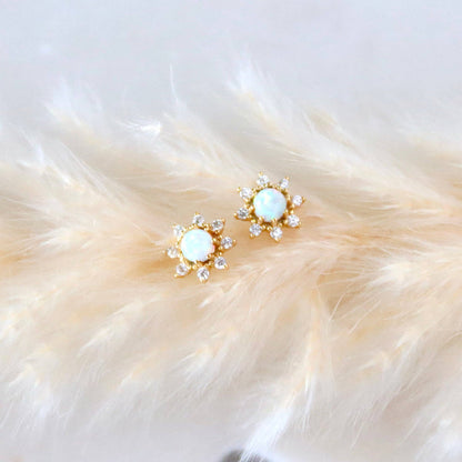 Pair of gold earrings with opal stones on a fluffy white surface