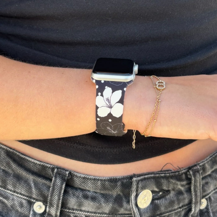Coconut Lane Mono Flora Apple Watch Strap on wrist, paired with a gold bracelet, black jeans, and a black top.
