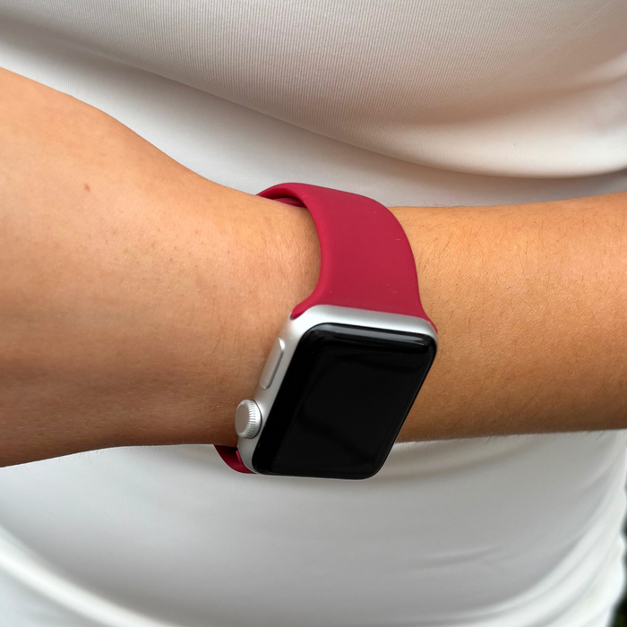 Coconut Lane NAKD Apple Watch Strap in cherry red, worn on a wrist with a white shirt in the background.