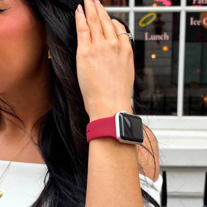 Woman wearing a cherry red Coconut Lane NAKD Apple Watch strap and a ring, hand raised near her face outdoors.