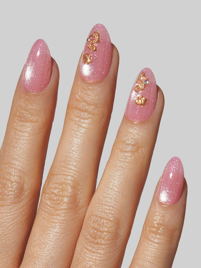 Hand with pink glittery nails and gold decorations on a light gray background