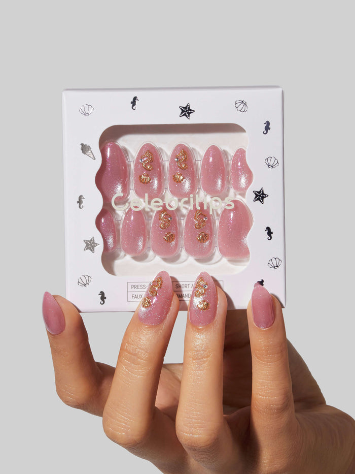 Set of pink Pose by the Beach press-on nails with gold decorations in a white box labeled 'Celebritips'.