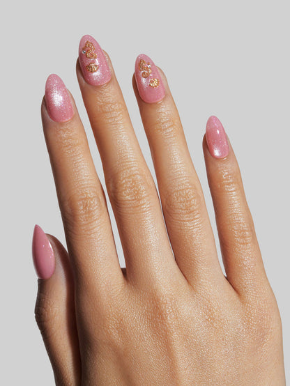 Hand with pink nails and gold decorations on a plain background