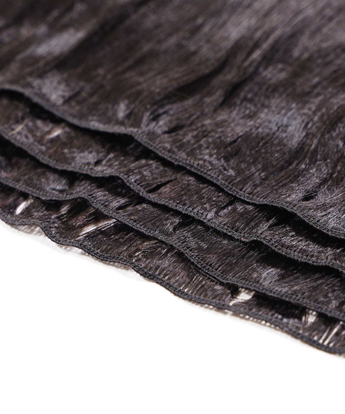 Close-up of several layers of black straight synthetic hair extensions, featuring visible stitching along the top edge on a white surface.