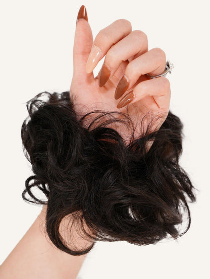A hand with long, manicured nails wears a Perfect Locks Scrunchie Hair Extension in Caramel Blonde  around the wrist. The thumb is up against a plain, light background.#color_natural-black-(1B)