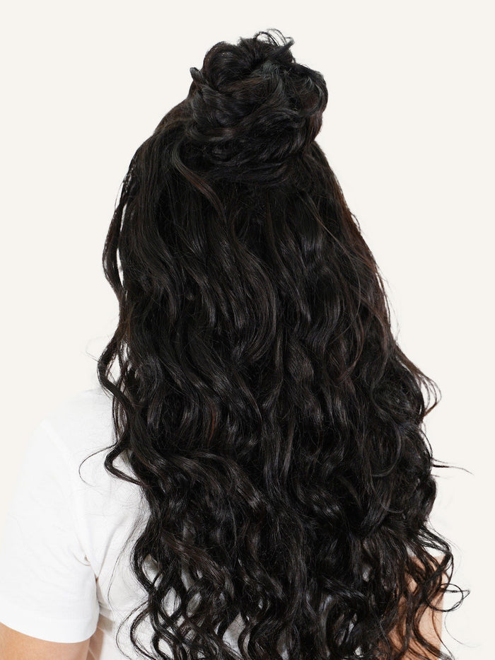 A person with long, wavy golden blonde hair in a half-up top knot, white shirt, back view, light background; color 613 scrunchie.#color_natural-black-(1B)