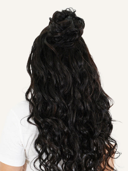 A person with long, wavy golden blonde hair in a half-up top knot, white shirt, back view, light background; color 613 scrunchie.#color_natural-black-(1B)