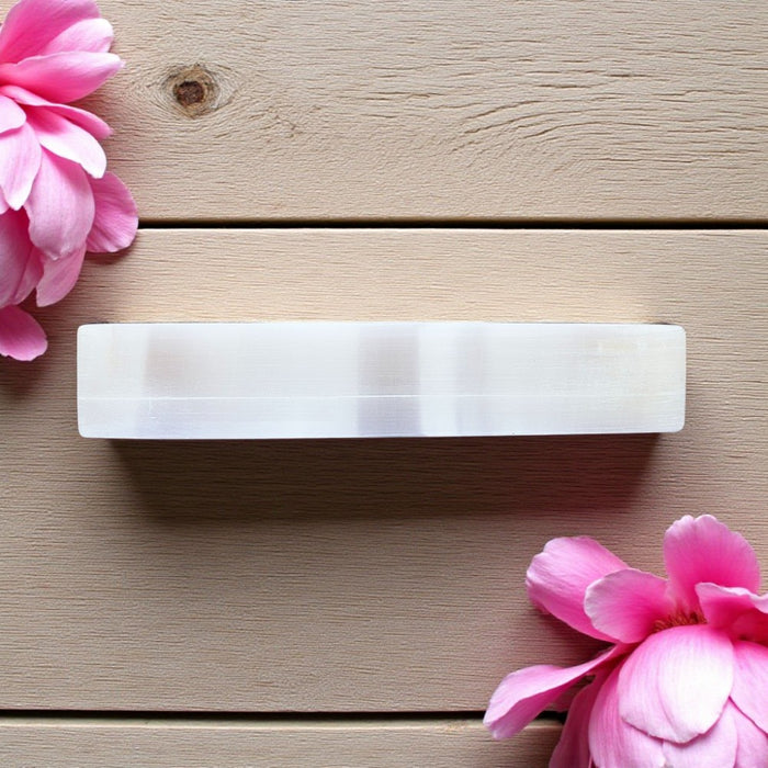 Rectangular white selenite charging bar on a wooden surface with pink flowers