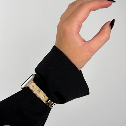 Gold shimmer star Apple Watch strap on wrist with black nails, shown over a black long-sleeve shirt.