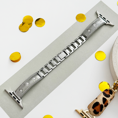 Silver Apple Watch strap with shimmering gold confetti details and a leopard print clip, displayed on a gray surface.
