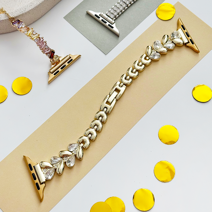 Gold Apple Watch strap with crystal accents on a beige card, scattered with gold confetti.