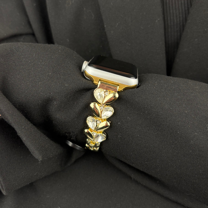 Gold Apple Watch strap with sparkle petal design displayed on black textured fabric.