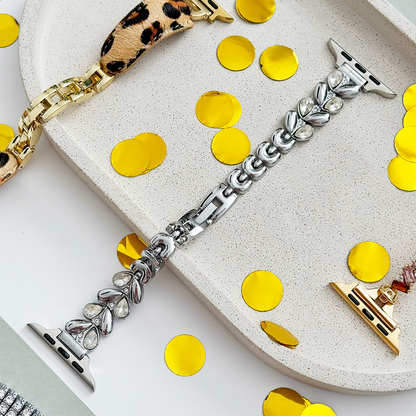 Silver Coconut Lane Sparkle Petal Apple Watch strap on a stone tray, with gold confetti dots and a leopard print band nearby.