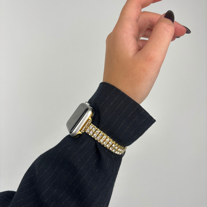Gold Coconut Lane Sparkle Season Apple Watch strap on wrist, dark pinstripe sleeve visible.