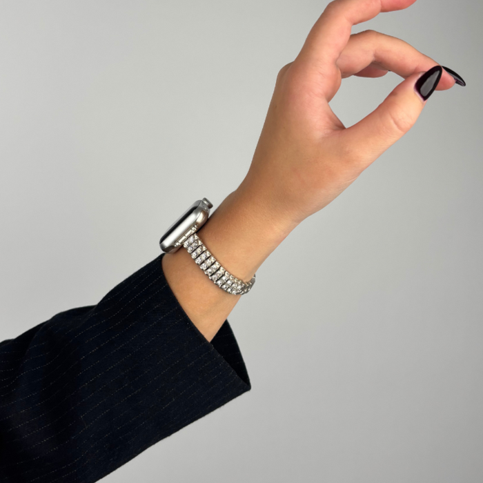 Hand with black nail polish wearing a silver Coconut Lane Sparkle Season Apple Watch strap and a silver bracelet.