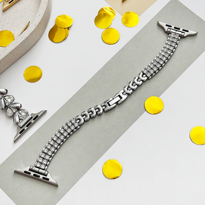 Silver Apple Watch strap with a glittery finish, displayed on gray background alongside gems and yellow confetti.