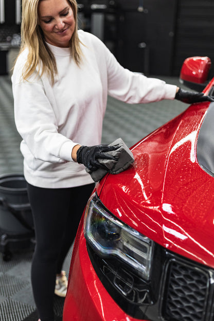 Person cleaning a red car with a black gloved hand with a grey sponge.