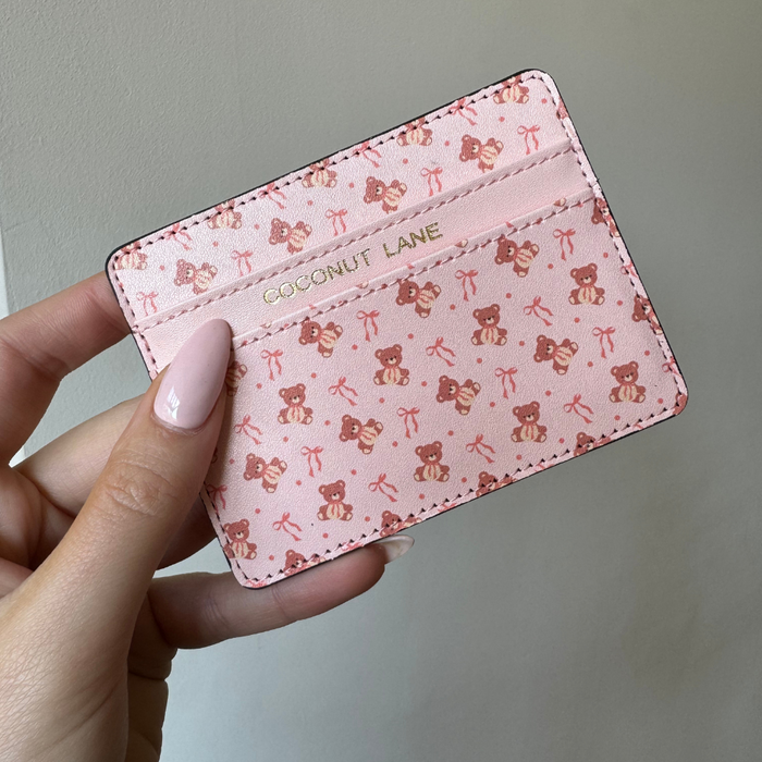 Pink Coconut Lane Thea Teddy Card Holder with teddy bear and bow print, gold lettering, held in a hand.